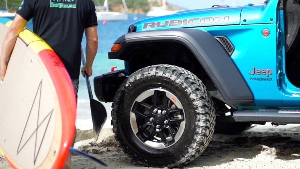 A turquoise jeep parked on the beach with a paddleboard, St. Thomas